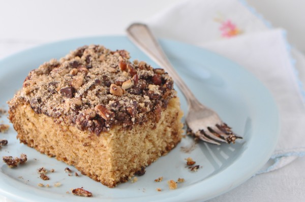 "Slice of coffee cake sitting on a light blue plate with a fork on the plate and crumbs scattered about"